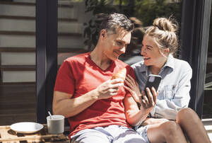 Ehepaar entspannt sich auf dem Balkon mit Smartphone - UUF30106
