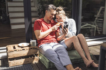 Ehepaar entspannt sich auf dem Balkon mit Smartphone - UUF30107