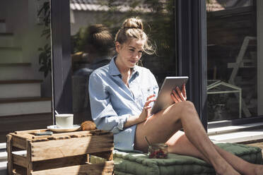 Woman relaxing on balcony with digital tablet in hands - UUF30112