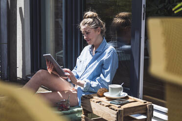 Woman relaxing on balcony with digital tablet in hands - UUF30114