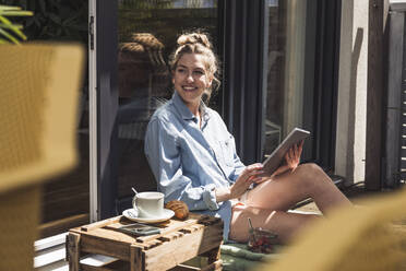 Woman relaxing on balcony with digital tablet in hands - UUF30115