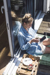 Porträt einer Frau, die sich auf einem Balkon mit einer Tasse und einem Smartphone in den Händen entspannt - UUF30120