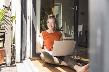 Porträt einer Frau, die mit einem Laptop auf einem offenen Balkon sitzt - UUF30125