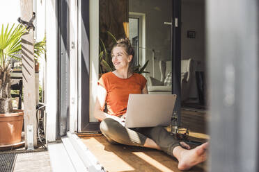 Portrait of woman sitting by open balcony with laptop - UUF30126