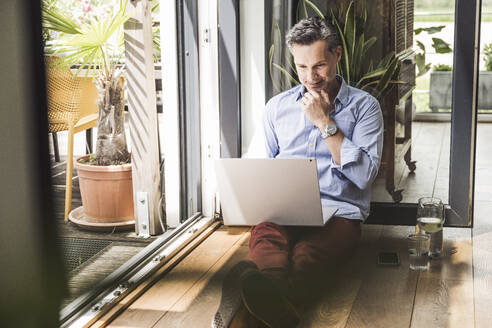 Portrait of man using laptop by open balcony - UUF30140