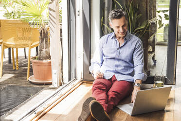 Portrait of man using laptop by open balcony - UUF30142