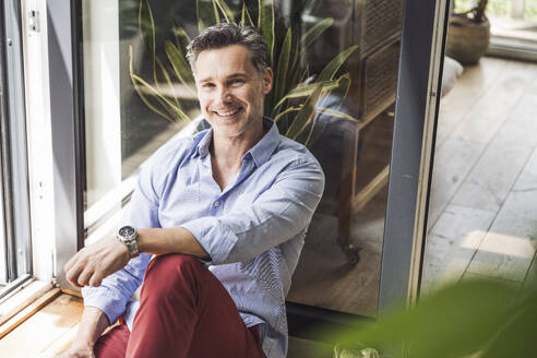 Portrait of man sitting by open balcony door - UUF30144