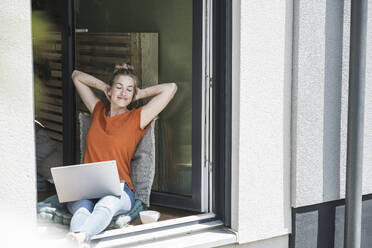 Woman relaxing by open window with laptop - UUF30148