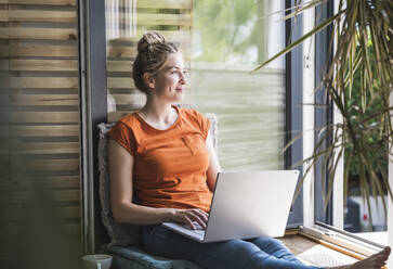 Porträt einer Frau, die sich auf einem Balkon mit einem Laptop entspannt - UUF30149
