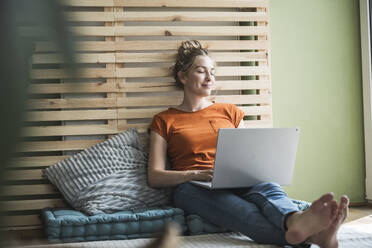 Porträt einer Frau, die auf einer Matratze sitzt und sich mit einem Laptop entspannt - UUF30151