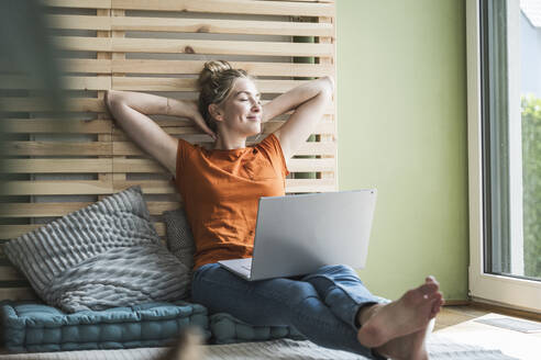 Portrait of woman sitting on mattress relaxing with laptop - UUF30152
