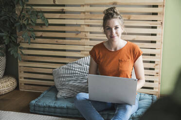 Porträt einer Frau, die auf einer Matratze sitzt und einen Laptop benutzt - UUF30153