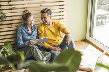 Couple sitting together on mattress using digital tablet - UUF30160