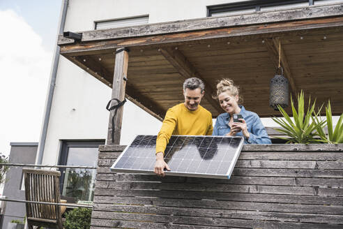 Ein Paar installiert ein Solarpanel auf einem Holzbalkon - UUF30166