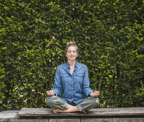 Portrait of woman meditating on bench in front of hedge - UUF30182