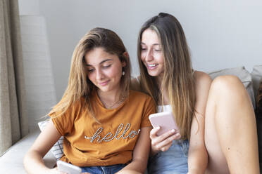 Lächelnde Freunde benutzen ihr Smartphone zu Hause - JPTF01263