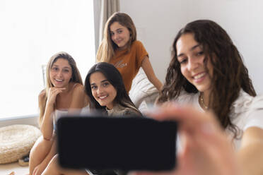 Happy friends taking selfie sitting on sofa at home - JPTF01267