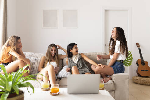 Friends sitting on sofa with laptop and laughing at home - JPTF01271