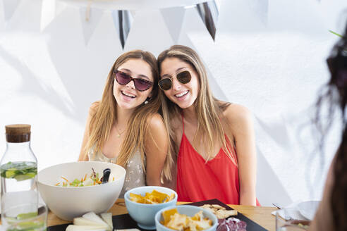 Smiling friends having lunch at table in front of wall - JPTF01276