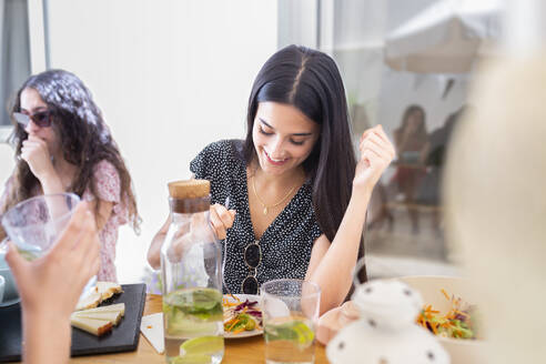 Lächelnde Frau beim Mittagessen mit Freunden am Tisch - JPTF01279