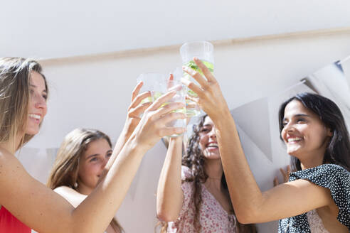 Smiling friends raising toast in front of wall - JPTF01280