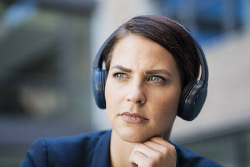 Nachdenkliche Geschäftsfrau hört Musik über kabellose Kopfhörer - JOSEF20706