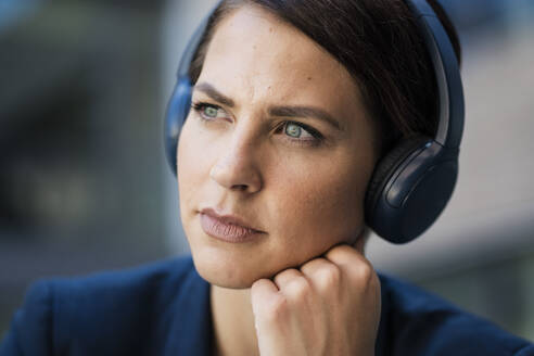 Nachdenkliche Geschäftsfrau hört Musik über kabellose Kopfhörer - JOSEF20709