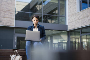 Businesswoman using laptop and sitting on bench - JOSEF20712