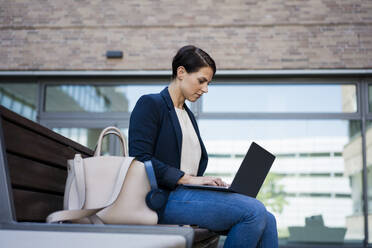 Konzentrierte Geschäftsfrau, die einen Laptop benutzt und auf einer Bank sitzt - JOSEF20713