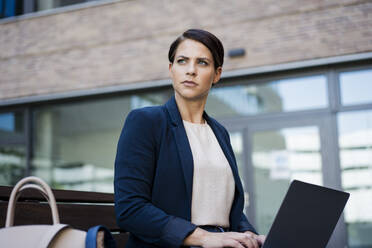 Thoughtful businesswoman sitting with laptop on bench - JOSEF20715