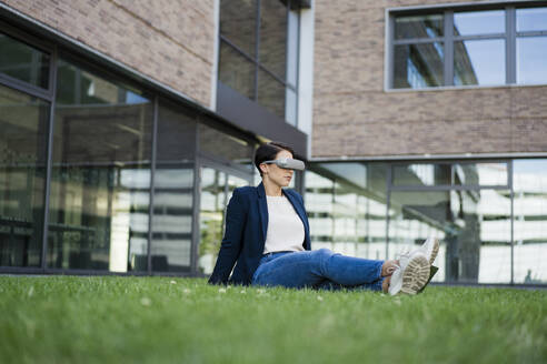Geschäftsfrau mit VR-Headset im Gras sitzend im Büropark - JOSEF20719