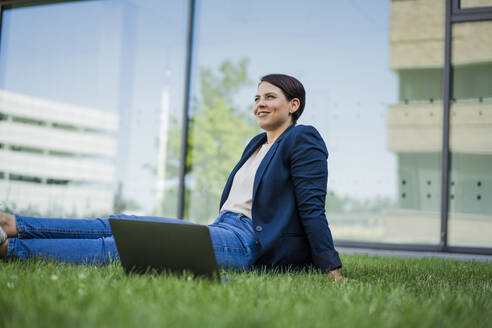 Lächelnde Geschäftsfrau mit Laptop im Gras sitzend - JOSEF20720