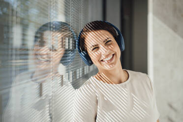 Happy businesswoman with wireless headphones in office - JOSEF20725