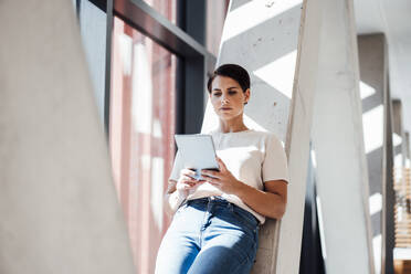 Businesswoman using tablet PC and leaning on column in office - JOSEF20737