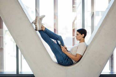 Businesswoman using tablet PC sitting on V-shaped column - JOSEF20740