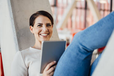 Happy businesswoman with tablet PC on V-shaped column - JOSEF20742