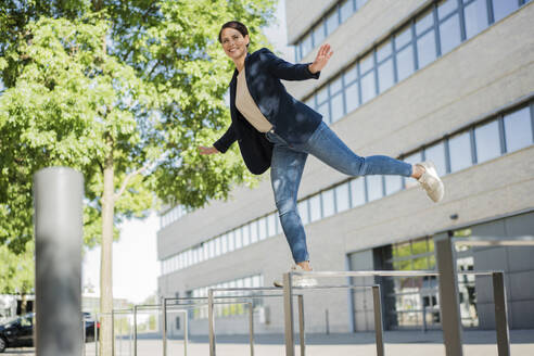 Businesswoman with arms outstretched balancing on railing - JOSEF20761