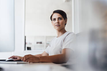 Confident businesswoman at desk in office - JOSEF20773