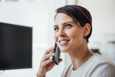 Lächelnde Geschäftsfrau, die im Büro mit einem Smartphone telefoniert - JOSEF20776