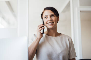 Lächelnde Geschäftsfrau, die am Arbeitsplatz mit einem Mobiltelefon spricht - JOSEF20777
