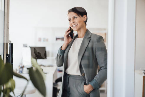 Glückliche Geschäftsfrau, die am Arbeitsplatz mit ihrem Smartphone telefoniert - JOSEF20792