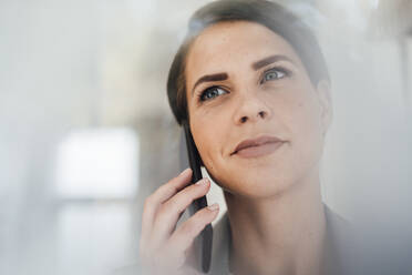 Contemplative businesswoman talking on smart phone at office - JOSEF20795