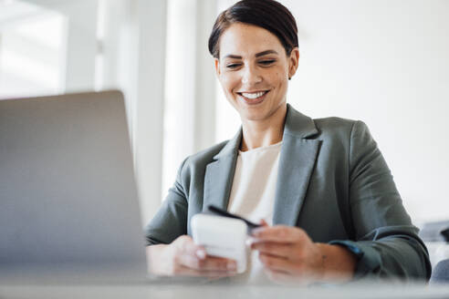 Lächelnde Geschäftsfrau, die eine Kreditkarte am Arbeitsplatz benutzt - JOSEF20798