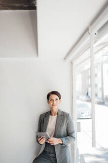 Businesswoman with tablet PC in front of wall at office - JOSEF20803