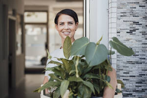 Lächelnde Geschäftsfrau mit Topfpflanze vor der Tür eines Büros - JOSEF20807
