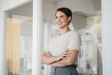 Smiling businesswoman with arms crossed standing in office - JOSEF20812