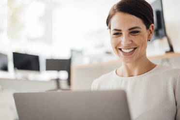 Smiling businesswoman using laptop at workplace - JOSEF20815