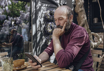 Mature man using smart phone at table in sidewalk cafe - OSF02116