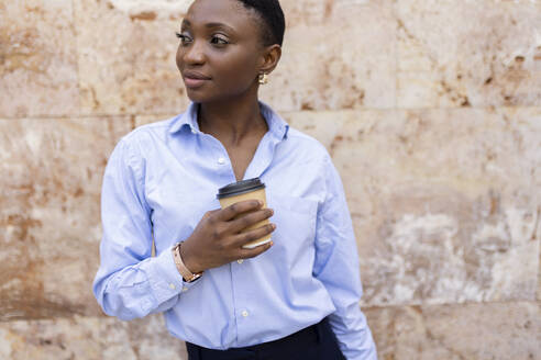 Smiling businesswoman with coffee cup standing in front of marble wall - JPTF01294