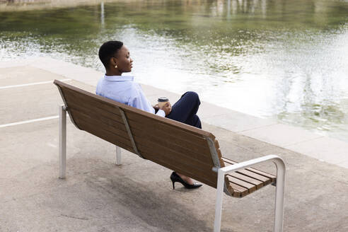 Thoughtful businesswoman sitting on bench in front of lake - JPTF01296